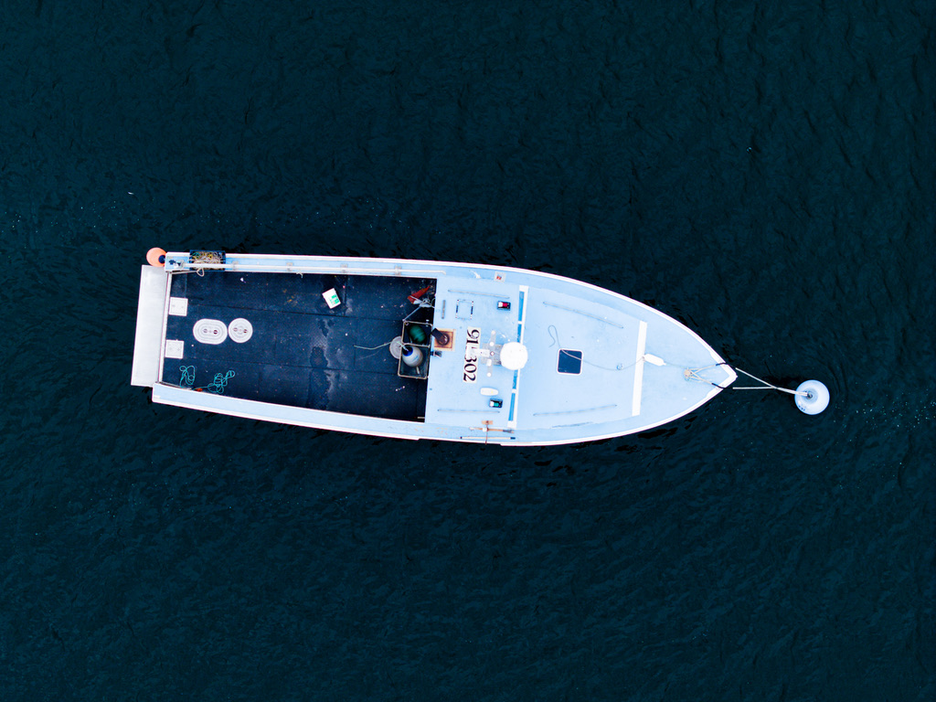 Aerial overhead photograph of a white working lobster boat hull number 91502 moored in Beverly Harbor Massachusetts