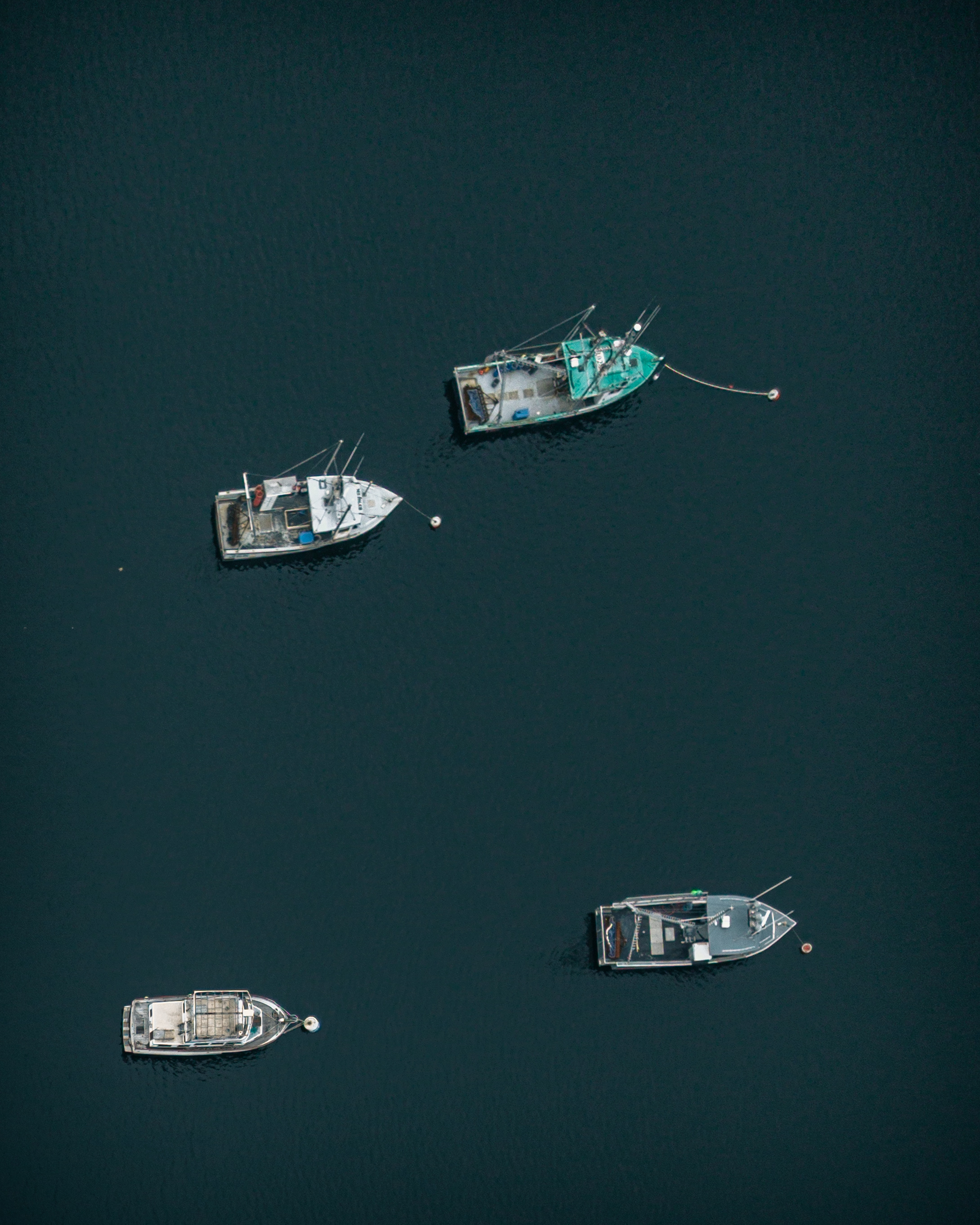 Aerial overhead photograph of four boats on moorings in Gloucester Harbor Massachusetts including one bright blue hull
