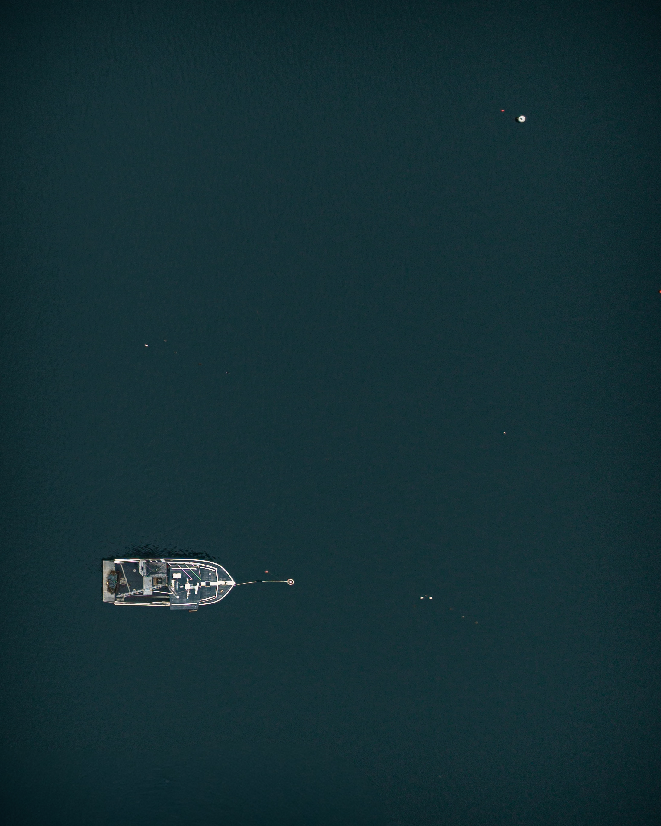 Aerial photograph of a single working boat moored alone on dark water in Gloucester Harbor Massachusetts after the 2026 scallop season closed