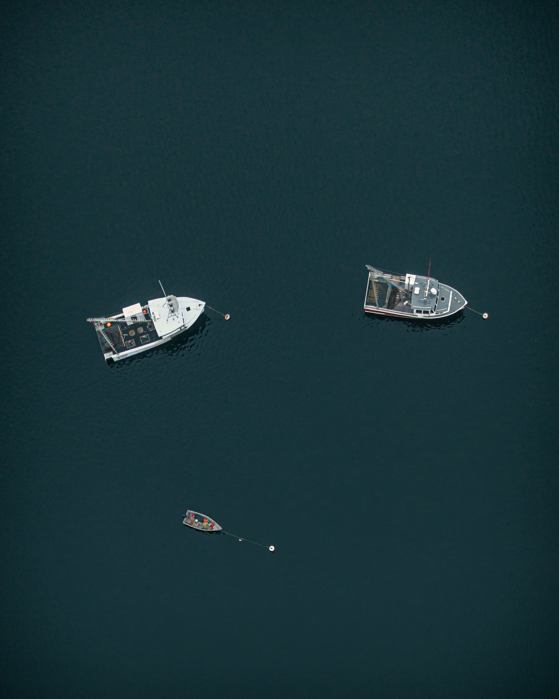 Aerial overhead photograph of two working boats and a small skiff moored on dark water in Gloucester Harbor Massachusetts